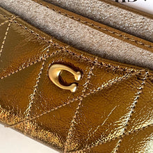 Load image into Gallery viewer, Close-up of a gold quilted leather wallet with a brand logo.
