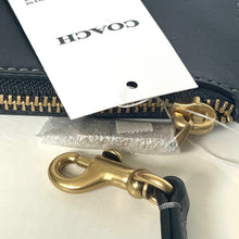 Load image into Gallery viewer, Close-up of a black leather wallet with gold zipper pull and hook, featuring Coach branding.