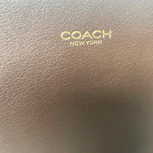 Load image into Gallery viewer, Close-up of a Coach New York product with gold logo on a brown leather surface.