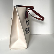 Load image into Gallery viewer, White tote bag with brown handle and black text on a white background