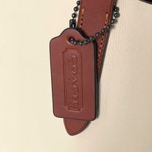 Load image into Gallery viewer, Coach leather tag on a strap against a beige background