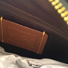 Load image into Gallery viewer, Close-up of a brown leather tag on a black bag with gold stitching.