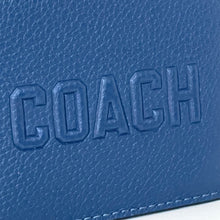 Load image into Gallery viewer, Close-up of a blue leather surface with &#39;COACH&#39; embossed on it.