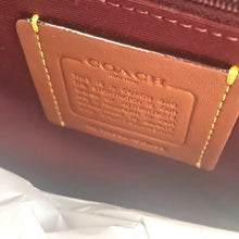 Load image into Gallery viewer, Close-up of a Coach logo on a maroon fabric background