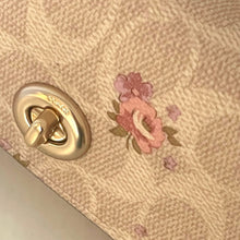 Load image into Gallery viewer, Close-up of a Coach handbag with floral design and gold clasp.