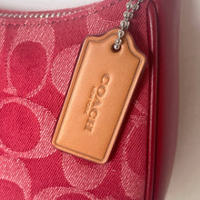 Load image into Gallery viewer, Close-up of a Coach wallet with a brown leather tag on a red patterned background