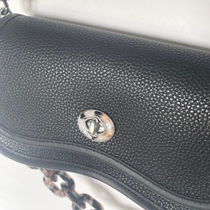 Close-up of a black textured handbag with a silver clasp on a white background