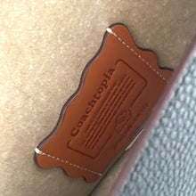 Load image into Gallery viewer, Brown leather tag with &#39;Coachcopia&#39; branding on a textured surface