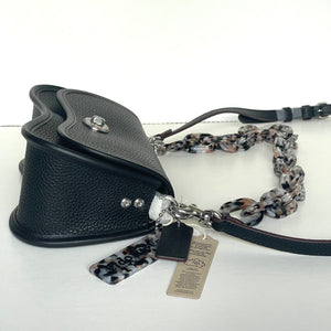 Black leather dog muzzle with a patterned leash and tag on a white background