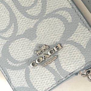 Close-up of a Coach wallet with logo charm and keychain on a light background