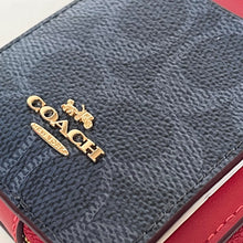 Load image into Gallery viewer, Close-up of a Coach logo on a textured surface with red accents.