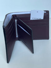 Load image into Gallery viewer, A dark brown leather Coach bi-fold wallet shown open, displaying its interior card slots, white lining, and a white paper tag with the Coach logo, set against a plain light background.
