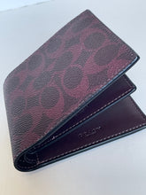 Load image into Gallery viewer, A Coach bi-fold wallet in the brand's signature monogram canvas, featuring a dark burgundy and black pattern with dark brown leather trim and interior, shown on a light gray surface.