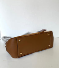 Load image into Gallery viewer, A brown leather handbag shown from its bottom corner, featuring gold-tone metal studs and a dust bag partially visible behind it, set against a plain white background.