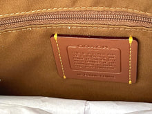 Load image into Gallery viewer, Close-up of a brown leather interior label with yellow stitching, embossed text, and a zipper in the background.