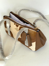 Load image into Gallery viewer, A Coach shoulder bag made of brown and cream cowhide with smooth brown leather trim, shown open with protective plastic wrapping still on the straps and tassel.