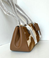 Load image into Gallery viewer, A structured shoulder bag with a brown smooth leather body and a brown-and-cream cowhide pattern panel, wrapped in protective clear plastic on the handles, set against a plain white background.
