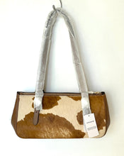Load image into Gallery viewer, A Coach handbag with a brown and cream cowhide pattern, featuring protective plastic wrapping on the handles and a white product tag.
