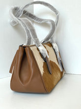 Load image into Gallery viewer, A small structured handbag with a brown faux-leather body and a cowhide-patterned front panel, featuring dual shoulder straps wrapped in protective clear plastic. The bag is photographed against a plain white background.