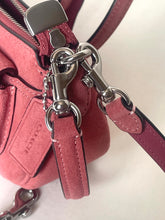 Load image into Gallery viewer, Close-up of a dusty rose suede handbag with silver-tone hardware, including a zipper pull, clasp, and strap attachments, with a Coach logo embossed on a leather tab.