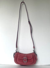 Load image into Gallery viewer, A dusty rose red leather shoulder bag with a front flap and silver buckle, hanging from a black hook against a plain white wall.