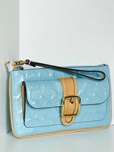 Load image into Gallery viewer, A light blue patent leather clutch bag with an embossed monogram pattern, a tan leather strap detail with a gold buckle, and a black wristlet strap.