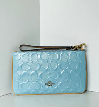 Load image into Gallery viewer, A light blue Coach wristlet clutch with an embossed signature 'C' pattern, a dark brown wrist strap, and gold-tone hardware, set against a white corner background.