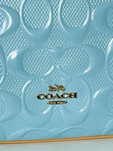 Load image into Gallery viewer, Close-up of a light blue Coach handbag featuring the signature embossed CC monogram pattern and a gold-tone Coach logo on the front.