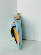 Load image into Gallery viewer, A light blue leather shoulder bag with tan leather trim and gold-tone hardware, shown standing upright against a white corner wall.