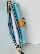 Load image into Gallery viewer, A light blue patent leather clutch or wallet-style handbag shown open, with a tan leather strap detail and gold-tone hardware, photographed against a plain white background.