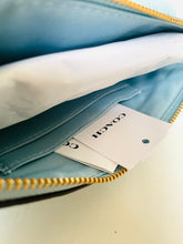 Load image into Gallery viewer, Close-up of an open Coach zip pouch showing a light blue interior, white tissue paper, and a white brand tag with the Coach logo.