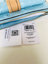 Load image into Gallery viewer, A Coach light blue patent leather zip-around wallet with a tan leather trim, shown with its retail price tag and barcode card on a light beige surface.