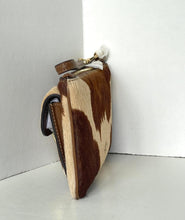 Load image into Gallery viewer, A small handbag made from brown and cream cowhide, standing upright in a white corner.