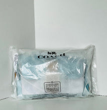 Load image into Gallery viewer, A Coach branded clear plastic bag containing a folded white and light blue textured fabric item, photographed against a plain white background.