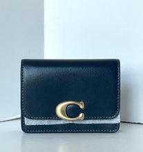 Load image into Gallery viewer, A Coach small wallet in navy blue leather with a signature gold 'C' logo clasp and a textured light gray fabric band across the front, shown on a light gray surface against a white background.