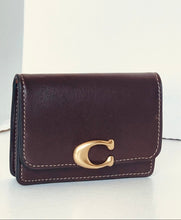 Load image into Gallery viewer, A dark brown leather wallet with white contrast stitching and a prominent gold-tone 'C' logo clasp on the front, set against a plain light background.