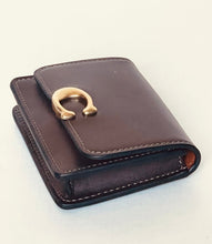 Load image into Gallery viewer, A dark brown leather wallet with a distinctive gold horseshoe-shaped metal clasp on the front flap, shown on a plain off-white background.