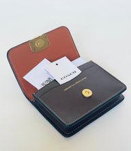 Load image into Gallery viewer, An open Coach wallet in dark brown and navy blue leather with gold-tone hardware, shown on a plain light background with a COACH paper tag visible inside.