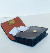 Load image into Gallery viewer, A Coach card holder wallet in dark navy blue and brown leather, shown open with a white brand tag attached. The wallet features a gold-tone snap button and a gold-tone lock on the inside flap.