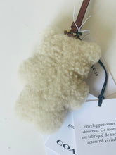 Load image into Gallery viewer, A fluffy cream-colored sheepskin or faux-shearling bag charm or accessory with a brown leather strap and gold-tone hardware, shown with branded white tags on a light background.