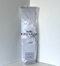 Load image into Gallery viewer, A Coach New York garment bag containing a white garment, photographed standing upright in the corner of a white room. The Coach logo is clearly visible on the front of the clear plastic bag.