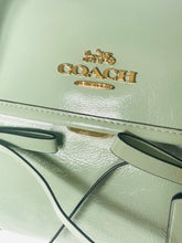 Load image into Gallery viewer, Close-up of a light green Coach handbag with gold logo.