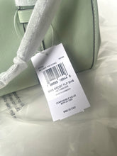 Load image into Gallery viewer, Close-up of a product tag on a light green leather bag.