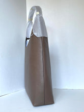 Load image into Gallery viewer, A brown leather tote bag with a silver metallic handle, standing upright against a plain white background.