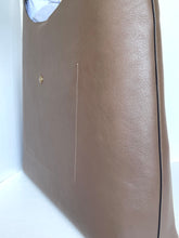 Load image into Gallery viewer, A close-up of a taupe brown leather tote bag with a small gold button detail and white contrast stitching, set against a plain white background.