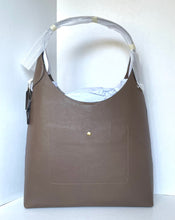 Load image into Gallery viewer, A taupe brown leather shoulder bag with a single top handle, featuring a front slip pocket with a small gold-tone snap button and a hangtag, photographed against a white background.