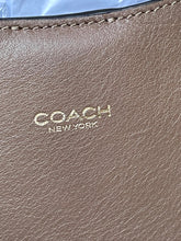 Load image into Gallery viewer, Close-up of a Coach New York textured leather pouch in taupe brown with gold foil branding.