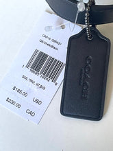 Load image into Gallery viewer, A black leather Coach luggage tag attached to a black strap, shown with its original white retail price tag on a light background.