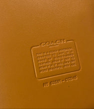 Load image into Gallery viewer, Close-up of a tan leather-like surface with an embossed Coach logo and product text reading 'THIS IS A COACH NOTEBOOK' and '216 52651 - CORDOVA'.