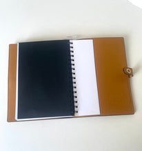 Load image into Gallery viewer, A tan leather spiral notebook cover shown open on a white surface, with a black notebook insert on the left, white pages in the center, and a tan leather back cover on the right with a small metal clasp.